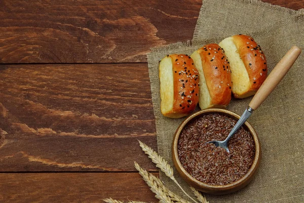 Kahverengi ahşap arka plan manzarası, fırın konsepti ve sağlıklı yiyecek ve diyet üzerine keten tohumlu keten peçetede ekmek ruloları kaşık ve kurutulmuş buğday demeti.