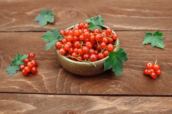 Tahta bir kâse içinde olgun, kırmızı ve sulu üzümlü meyveler kahverengi ahşap bir masa üzerinde yeşil yapraklar, vitamin dutları ve turta dolgusu kavramı.