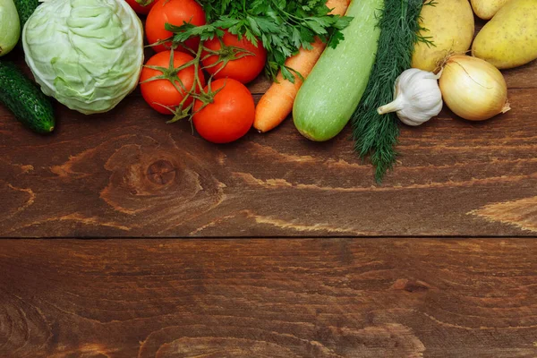 Çiğ sebze, salatalık, lahana, dalda domates, havuç, kabak, soğan, sarımsak, patates ve kahverengi ahşap arka planda bir demet maydanoz, sağlıklı gıda konsepti, çiğ gıda ve sebze yahnisi malzemeleri.