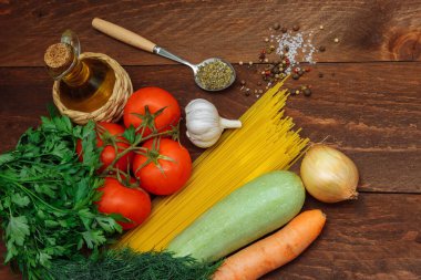  Çiğ sebze, sarımsak, havuç, domates, kabak, dereotlu spagetti. Bir kaşıkta maydanoz ve baharat, tuz ve biber ve kahverengi ahşap arka planda bir şişe zeytinyağı. 