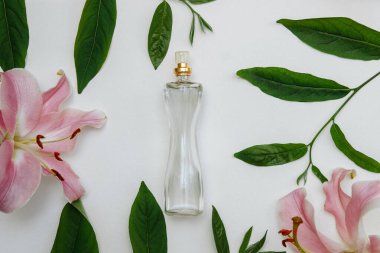 Şeffaf cam şişedeki parfüm şişesinde pembe zambak çiçekleri ve yeşil yapraklar beyaz arka planda, güzellik, tarz, özgüven kavramı.