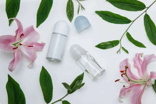  Şeffaf cam şişede paten deodorantları yeşil yapraklı ve pembe çiçekli açık ve kapalı kapaklı beyaz arka plan manzaralı, cilt bakımı konsepti, ter koruması ve reklamcılık. 