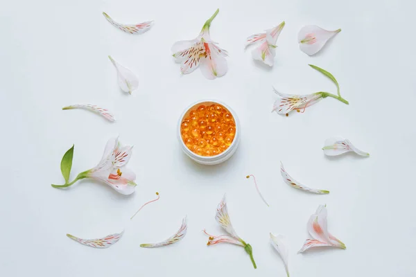 Sarı yuvarlak ve şeffaf yağ kapsülleri, vitaminler ve balık yağı ile beyaz bir kavanozda, çiçek ve taç yaprakları üst görünümde, cilt suyu ve besin konsepti, sağlık ve güzellik