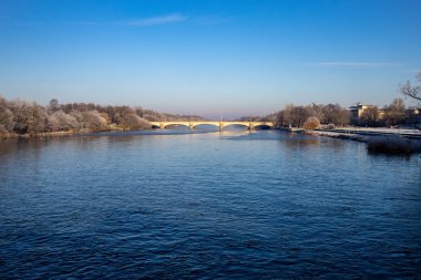 Ağaçlar ve mavi gökyüzü, weir ile kısmen donmuş nehir 