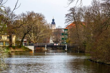 Leipzig'de ağaçlar ve arka planda Yeni Belediye Binası ile nehir üzerinde bir köprü görünümü