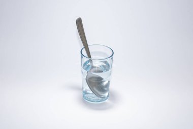 Cam bardakta metal kaşık, beyaz arka planda su var.