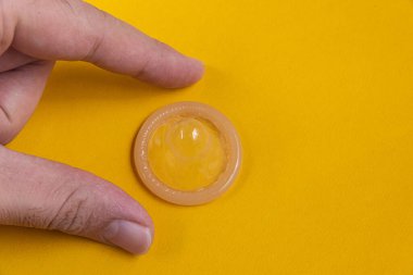 Sarı arka planda lateks prezervatif tutan adam.