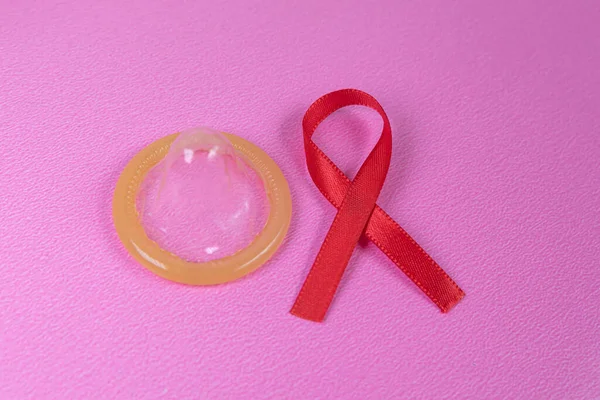 粉色背景上的红丝带和乳胶避孕套 — 图库照片