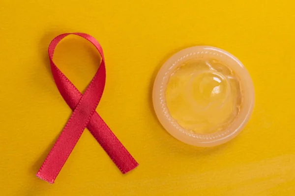 黄色背景上的红丝带和乳胶避孕套 — 图库照片
