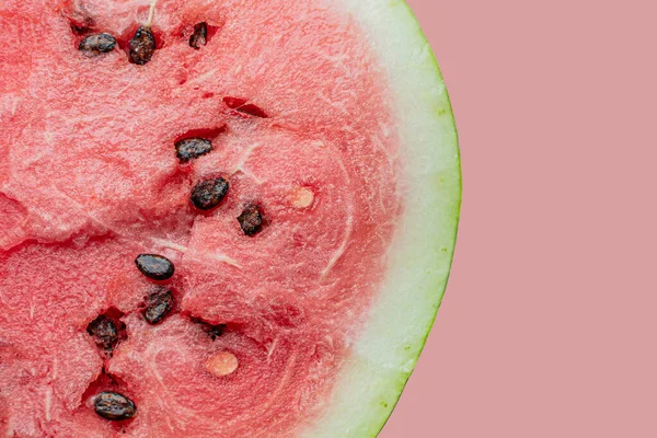 Pembe arka planda siyah çekirdekli olgun karpuzun yarısı.