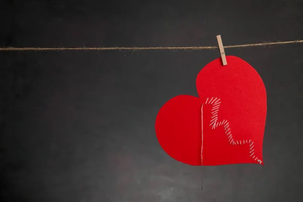 Sv. Valentine's background. Sewed up broken heart hanging on rope on dark background with copy space.