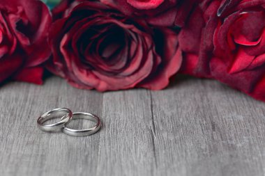 İki Alyans kopya alanı ahşap arka plan üzerinde kırmızı gül çiçekler Buket ile. Sevgililer günü