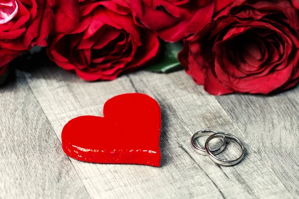大红色的心形状和结婚戒指与红玫瑰花在木背景 情人节明信片 — 图库照片