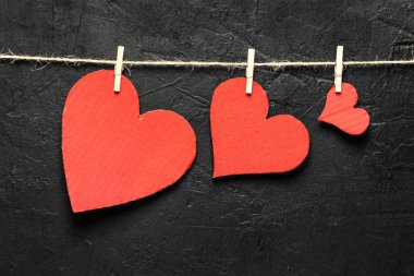 Üç küçük / büyük / büyük kalpler kopya alanı siyah arka plan üzerine ipte asılı. Sevgililer günü