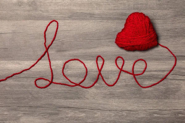 Handmade knitted red wool heart with love wool text on wooden background