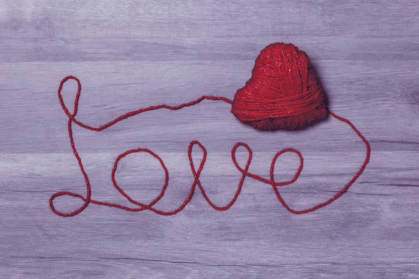 Handmade knitted red wool heart with love wool text on wooden background