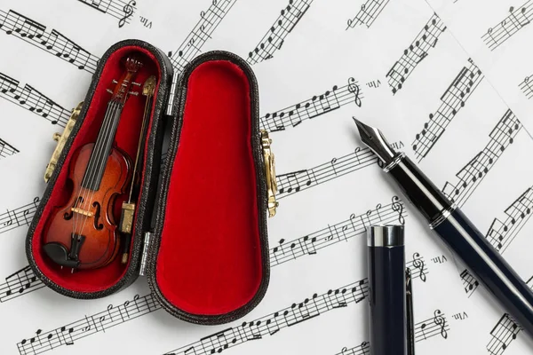 Violin inside red fiddle case and pen on music note paper background with copy space