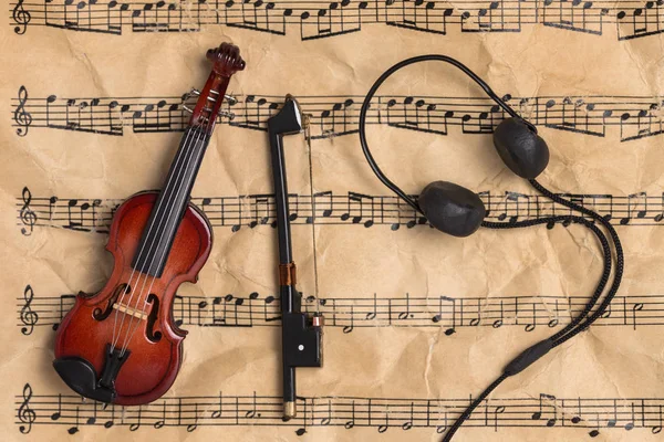 Violin and headphones on vintage music notes paper with copy space. Music background