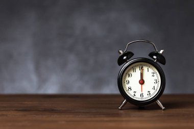 Saat 6 yönünde 12 alarmı var. Koyu arka planda kopya alanı ile ahşap masada Vintage/Retro siyah analog çalar saat