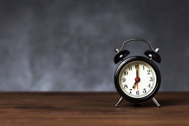 Saat 6 yönünde 7 ' de alarm var. Koyu arka planda kopya alanı ile ahşap masada Vintage/Retro siyah analog çalar saat