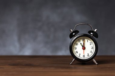 Saat 6 yönünde saati 11 alarmda. Koyu arka planda kopya alanı ile ahşap masada Vintage/Retro siyah analog çalar saat