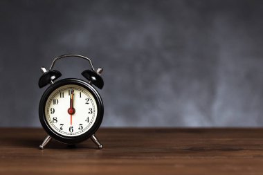Saat 6 yönünde 12 alarmı var. Koyu arka planda kopya alanı ile ahşap masada Vintage/Retro siyah analog çalar saat
