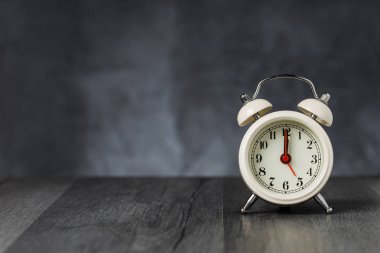 Saat 5 ' te saati 12 ' de alarmda. Koyu arka planda kopya alanı ile ahşap masada Vintage/Retro beyaz analog çalar saat