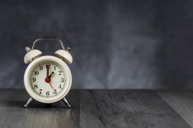 Saat 1 saat 5 yönünde alarm. Koyu arka planda kopya alanı ile ahşap masada Vintage/Retro beyaz analog çalar saat