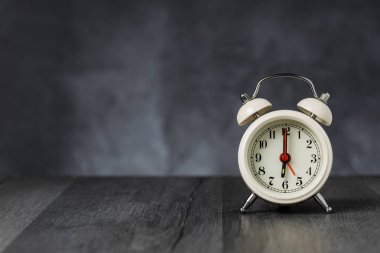Saat 5 yönünde alarm saati 6 ' da. Koyu arka planda kopya alanı ile ahşap masada Vintage/Retro beyaz analog çalar saat