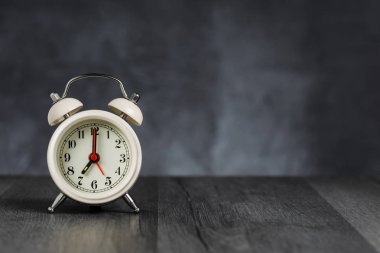 Saat 5 ' te saati 7 ' de alarmda. Koyu arka planda kopya alanı ile ahşap masada Vintage/Retro beyaz analog çalar saat