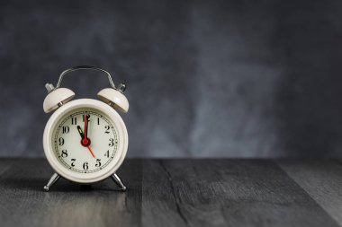 Saat 5 ' te saati 11 ' de alarmda. Koyu arka planda kopya alanı ile ahşap masada Vintage/Retro beyaz analog çalar saat