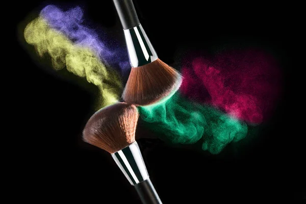 Eyeshadow explosion. Colourful face powder and two make-up cosmetic brushes isolated on black background.