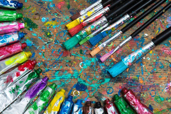 顶部视图 旧染色艺术家表与丙烯酸漆管和画笔 艺术背景 — 图库照片