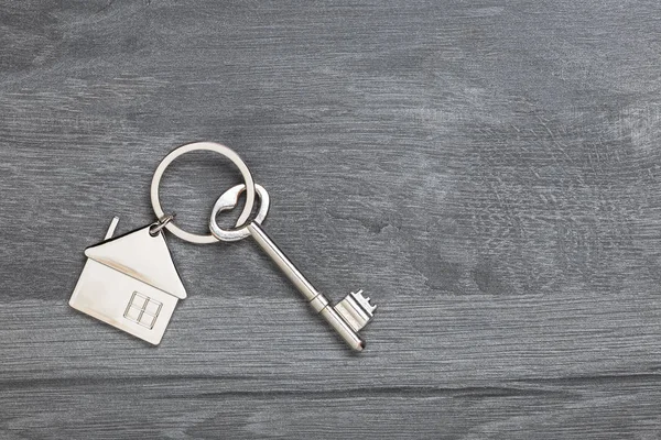 House keychain and vintage key on wooden table with copy space