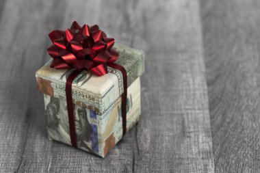 Hediye kutusu 100 Amerikan doları banknot ve kopya alanı ile ahşap masa üzerinde kırmızı kurdele sarılmış