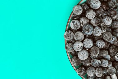 Kopya alanı ile turkuaz arka plan üzerinde taze dondurulmuş yaban mersini ile Yarım kase