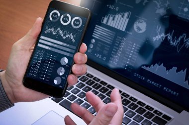 Yatırımcı borsa raporu ve finansal gösterge tablosu ile iş zekası (BI), anahtar performans göstergeleri (KPI) ile analiz. Dizüstü bilgisayar ile akıllı telefon kullanan iş adamı.