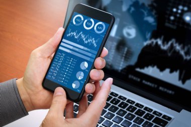 Yatırımcı borsa raporu ve finansal gösterge tablosu ile iş zekası (BI), anahtar performans göstergeleri (KPI) ile analiz. Dizüstü bilgisayar ile akıllı telefon kullanan iş adamı.