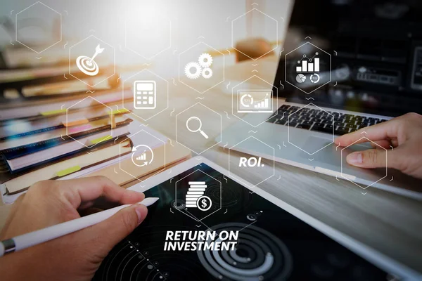 Yatırım getirisi getirisi yatırım göstergesi iş geliştirmek için sanal tablosu içinde. tasarımcı el kavram olarak ahşap masa üzerinde dijital tablet ve laptop bilgisayar ve kitap yığını ve göz cam ile çalışma