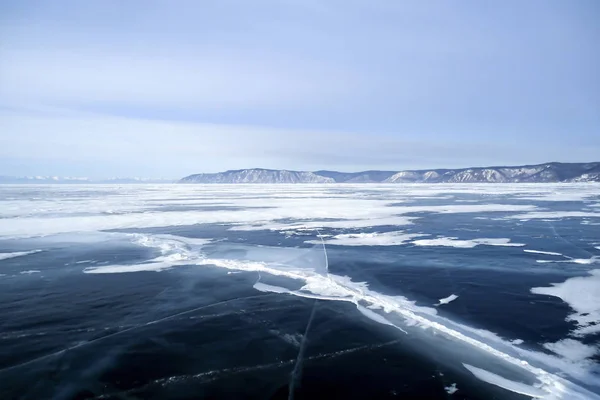 世界で最も深いバイカル湖のある素晴れしい冬景色暗い青氷の厚さひび付着 氷の小さな作品遠くの岩の多い海岸 冷ややかな朝もやの空ロシア — ストック写真