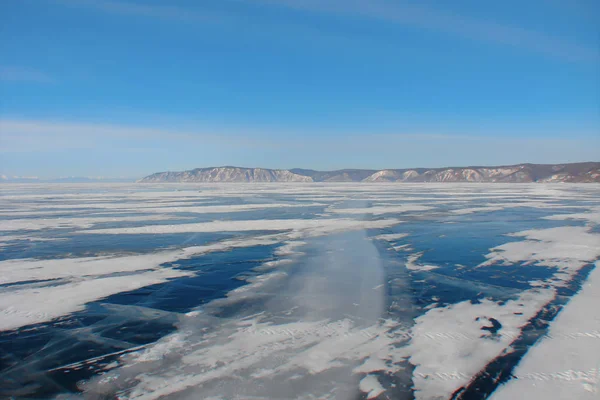 美味的景观与冬季道路通过冰冻的湖泊到一个遥远的岩石海岸 在破裂的深蓝色冰上的极端驾驶路线 天空在早晨冰凉的阴霾 — 图库照片