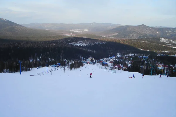 ski resort facilities at the foot of mountain slope; long downhill route; scenic landscape with boreal forest in a vast valley; undulating mountain range; top view