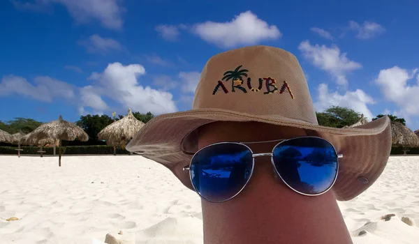 sun glasses and Aruba hat on a leg. Eagle beach on background