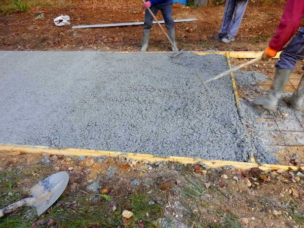 Beton bir garaj yolunun inşaatında yeni dökülmüş çimentoyu dengeleyen işçiler