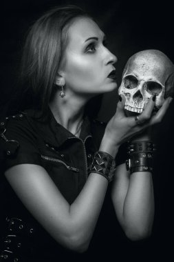 Heavy metal girl with skull posing over dark background clipart