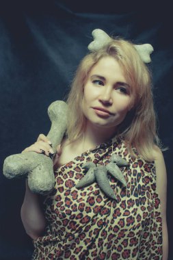 Karanlık arka planda poz veren tarih öncesi kadın. Kocaman bir kemik.