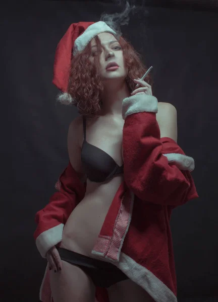 诱人的性感女孩在圣诞老人的服装吸烟在黑暗的背景 — 图库照片