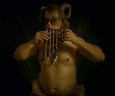 Horned faun with panflute posing over dark background clipart