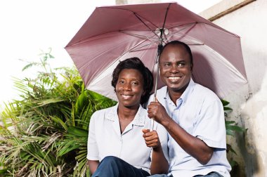 oturma ve kendisini bir çiçek yakınındaki bir şemsiye ile korumaya mutlu yetişkin çift.