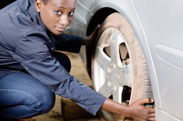 Young woman mechanic squatting near a car removes her tire.